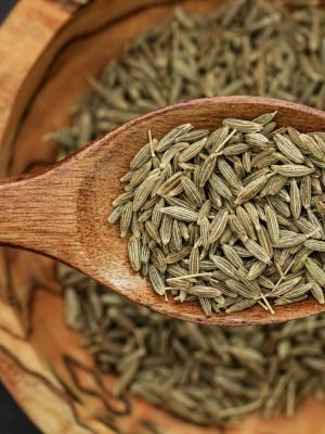 Home Detailed image of cumin seeds on a wooden spoon for culinary use.